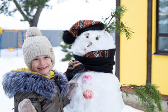 A child paints a snowman's face with paints - winter entertainment and creativity, sculpting a snowman in winter outdoor.