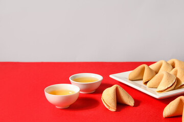 Plate with fortune cookies and cups of tea on table near light wall. Chinese New Year celebration