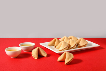 Plate with fortune cookies and cups of tea on table near light wall. Chinese New Year celebration