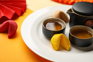 Plate with fortune cookies, teapot and cups on color background, closeup. Chinese New Year celebration