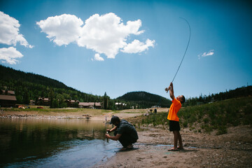 Boy catches fish from lake in mountain on vacation with dad