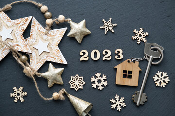 House key with keychain cottage on black background with stars, snowflakes. Happy New Year 2023-wooden letters, greeting card. Purchase, construction, relocation, mortgage