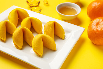 Plate with fortune cookies and mandarins on yellow background, closeup. Chinese New Year celebration