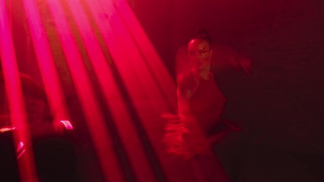 Woman in stage mini dress dances passionate Latin American tango dance in light of red laser with male partner, part of dance performance in dark with moving beams, swinging arms, turns,hugs in loft.