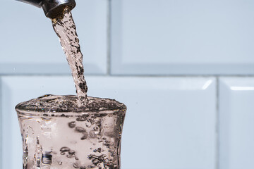A strong jet of water from a tap pours with splashes into a glass glass, the ecological value of...