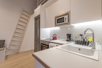 Studio apartment with open kitchen with white cabinets, wooden staircase and stainless steel appliances
