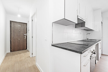 Kitchen open to the living room with white furniture with a black countertop and a corridor with an access door