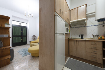 Kitchen without doors with bright wood cabinets, white appliances and access to a living room with a yellow sofa