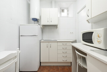 Small kitchen with white cabinets with a hot water heater, white fridge and microwave oven