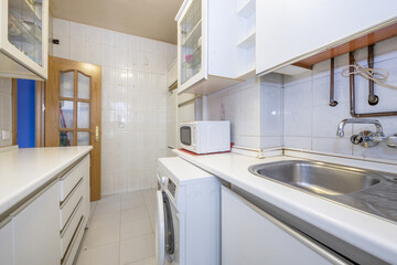 Kitchen with white furniture, countertops and appliances, copper water and gas pipes and oak wood door with beveled glass