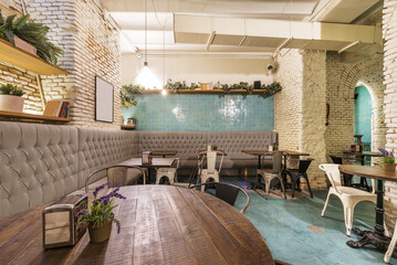 Living room of a restaurant with a sofa running along the entire perimeter with industrial-style furniture and white brick walls