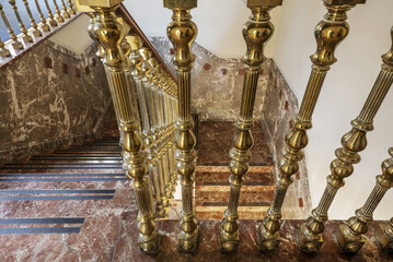 Stairs of a palace with brown marble and railing with golden metal balustrade