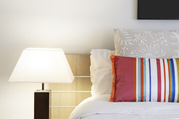 Detail of the headboard of a bedroom with cushions of combined colors and a lamp with a white fabric lampshade