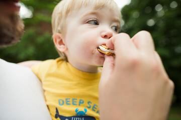 Cropped image of father feeding son smore in backyard