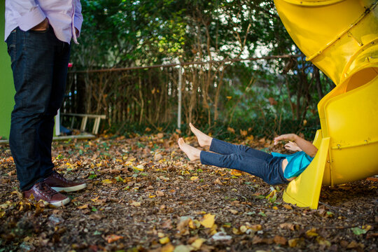the bottom half of a child emerges from a slide as her father watches