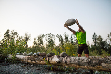 Ripped man throws giant boulder during an outdoor workout.