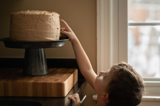 Little boy sneaking a taste of chocolate frosting from a homemade cake