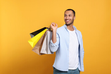 Happy African American man with shopping bags on orange background