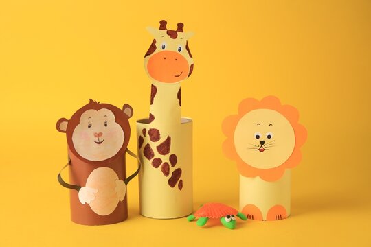 Toy monkey, giraffe and lion made from toilet paper hubs with plasticine turtle on yellow background. Children's handmade ideas