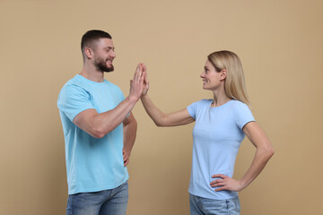 Happy couple giving high five on light brown background