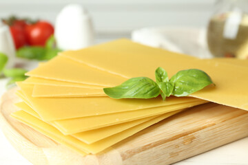 Uncooked lasagna sheets and basil on white wooden table, closeup