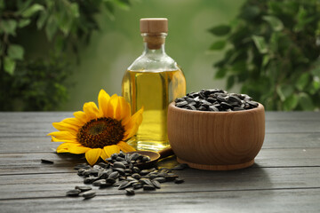 Sunflower, bottle of oil and seeds on wooden table against blurred background