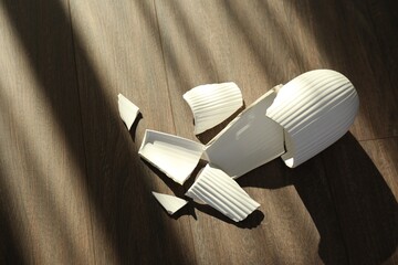 Broken white ceramic vase on wooden floor, above view