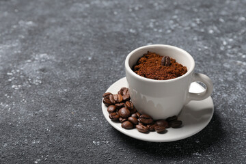 Cup with roasted beans and ground coffee on dark grey table. Space for text