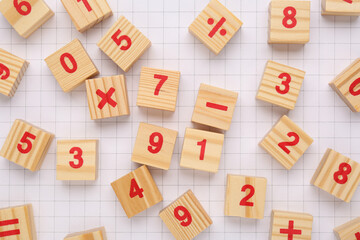 Wooden cubes with mathematical symbols and numbers on sheet of grid paper, flat lay