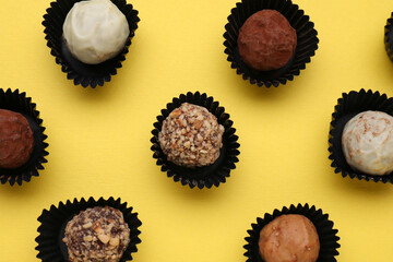 Different tasty chocolate candies on yellow background, flat lay