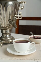 Vintage samovar and cup of hot drink served on white wooden table. Traditional Russian tea ceremony