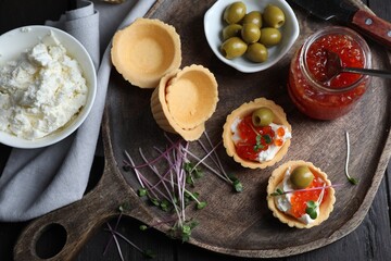 Delicious tartlets with red caviar and cream cheese served on wooden table, flat lay