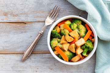 Food healthy stir fried chicken add broccoli carrot in bowl on wood table.