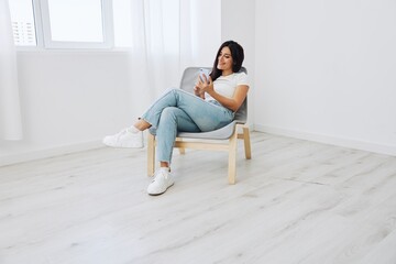 Woman sitting on chair with phone in hand in new apartment, online shopping via phone, online shopping