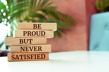 Wooden blocks with words 'Be proud but never satisfied'.