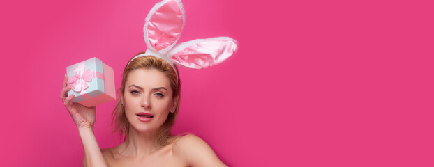 Obraz na płótnie Canvas Portrait of a happy Easter girl holding present box isolated over pink background. Young woman with bunny ears. Easter banner, mockup copy space, header for website, template.