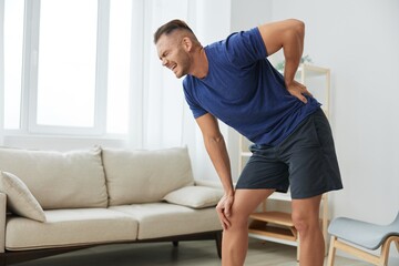 Man backache neck and shoulder pain, inflammation of muscles and ligaments rupture during sports, inflammation and injury, in a blue t-shirt at home