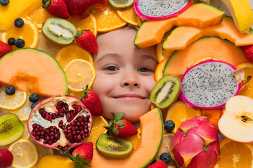 Happy smiling child face with fruits. Kids face with mix of strawberry, blueberry, strawberry, kiwi, dragon fruit, pomegranate, orange and melon. Assorted mix of fruits near child face.