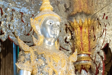 Deity statue standing straight made of silver, wearing silver gold costume with Chada on top of his head. Surrounded by sparkleling decoration.