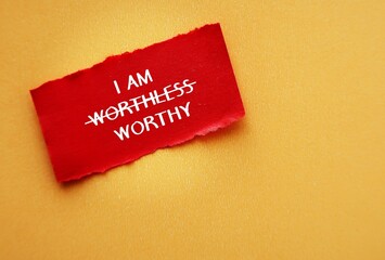 Torn red paper on copy space yellow background with text I AM WORTHLESS change to I AM WORTHY,...