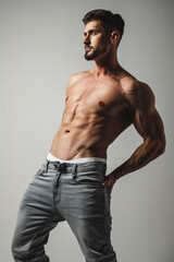 Male model with perfect body in jeans posing over grey background. Close-up. Studio shot.