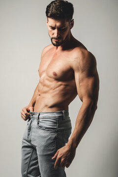 Male model with perfect body in jeans posing over grey background. Close-up. Studio shot.