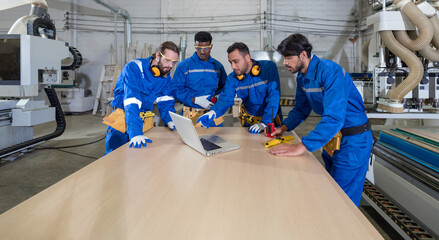 Group of multiethnic technicians in blue mechanic jumpsuits meeting,  using laptop computers on...