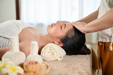 Obraz na płótnie Canvas Calm and peaceful Asian woman getting facial treatment massage by a professional masseur