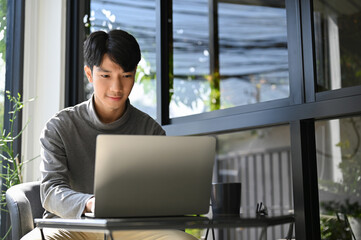 Smart Asian businessman remote working at the coffee shop, concentrating on his task on laptop