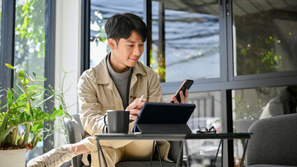 Happy and relaxed Asian an using his phone and portable tablet at the coffee shop. remote working