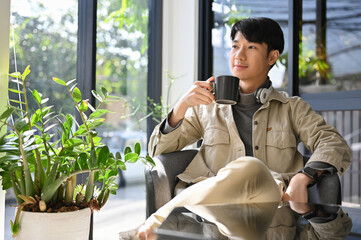 Fototapeta premium Successful Asian male enjoys having morning coffee at the coffee shop, daydreaming