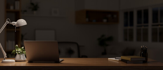 Dark workspace at night with laptop, stationery, table lamp, and decor on wood tabletop