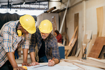 Two carpenter man wear helmet meeting planning job together at carpentry workshop, craftsmen talking checklist and plan on blueprint paper in woodshop, teamwork, National Carpenters Day