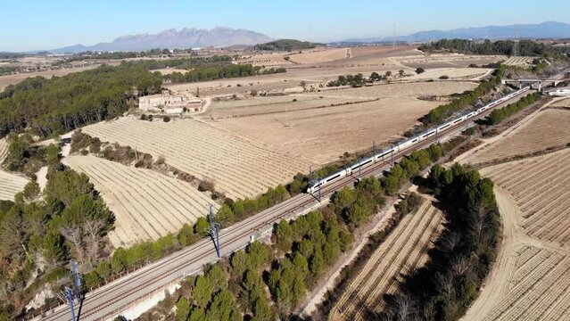 Aerial: high-speed train in Spain, travelling between Barcelona and Madrid, in the catalan countryside and Montserrat mountain range in the blackground